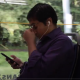 student riding bus, holding phone, rubbing his eyes